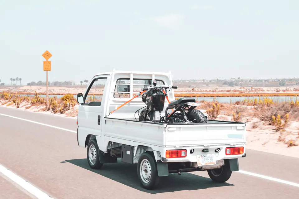 Honda Acty Kei Truck driving on a coastal highway with a dirt bike in the bed