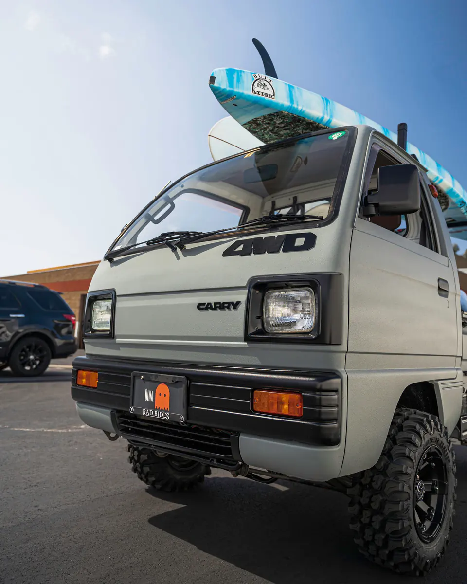 Lifted vintage Suzuki Carry 4WD on off-road tires with a ladder rack carrying paddleboards