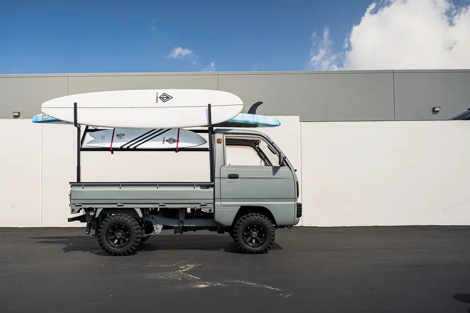 Side view of a lifted Suzuki Carry Kei Truck with a bed ladder rack and black wheels