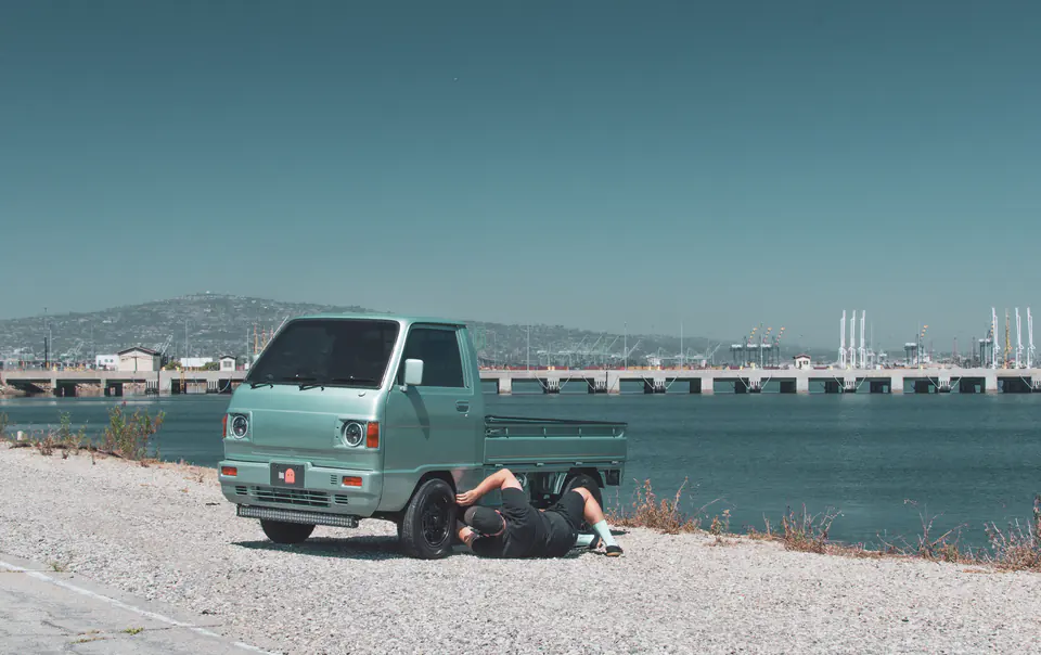 Mechanic working under a mint green vintage Honda Acty Kei Truck by the water