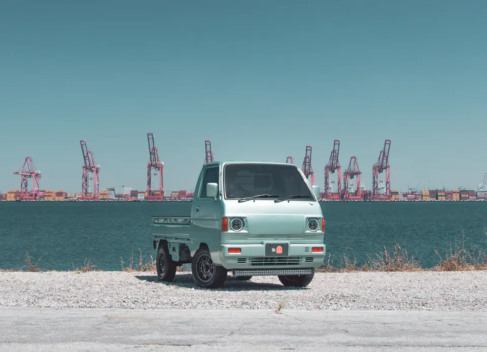 Mint green vintage Honda Acty Kei Truck parked in front of container cranes at a California port