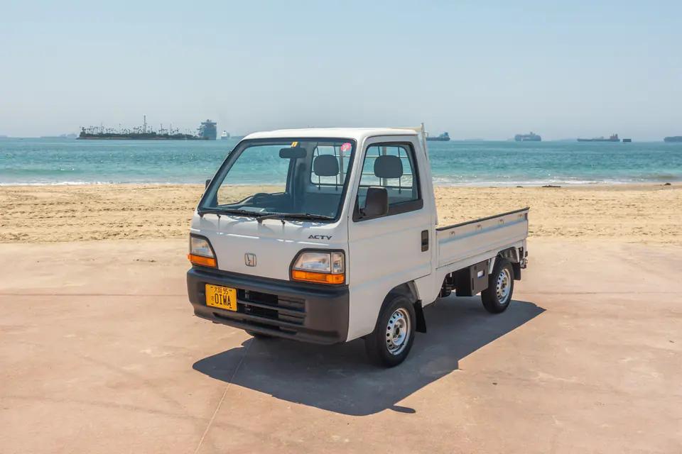 White 1990s Honda Acty Kei Truck with a yellow Japanese Kei license plate on the beach